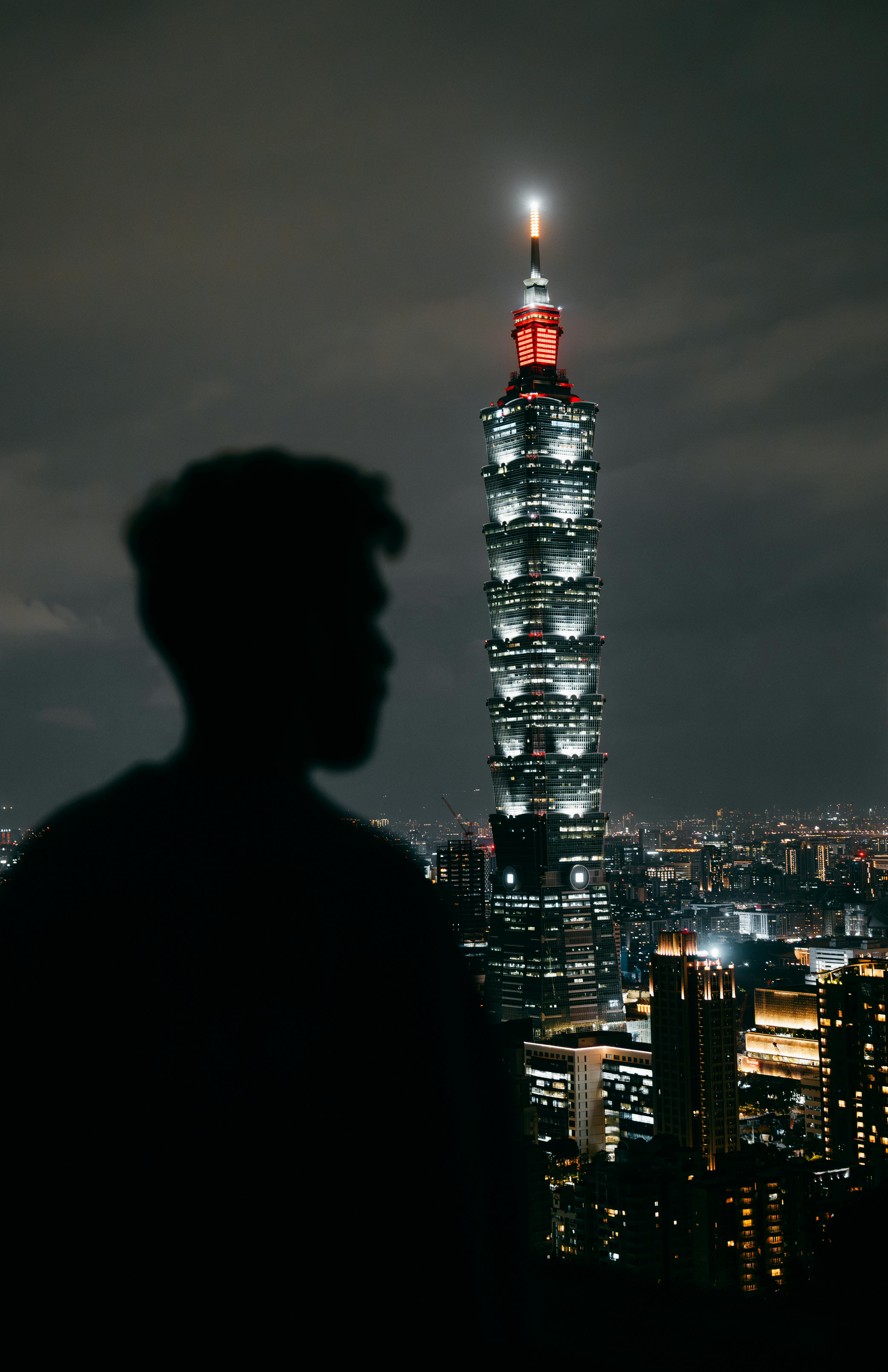 A silhouetted figure stands before Taipei 101, illuminated against the night cityscape.