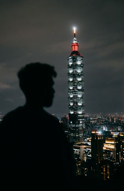 A silhouetted figure stands before Taipei 101, illuminated against the night cityscape.