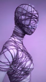 Conceptual artwork featuring a mannequin enveloped in purple string against a pink background.