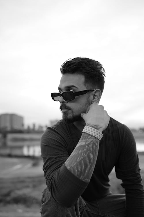 A man with tattoos and sunglasses sitting on a bench
