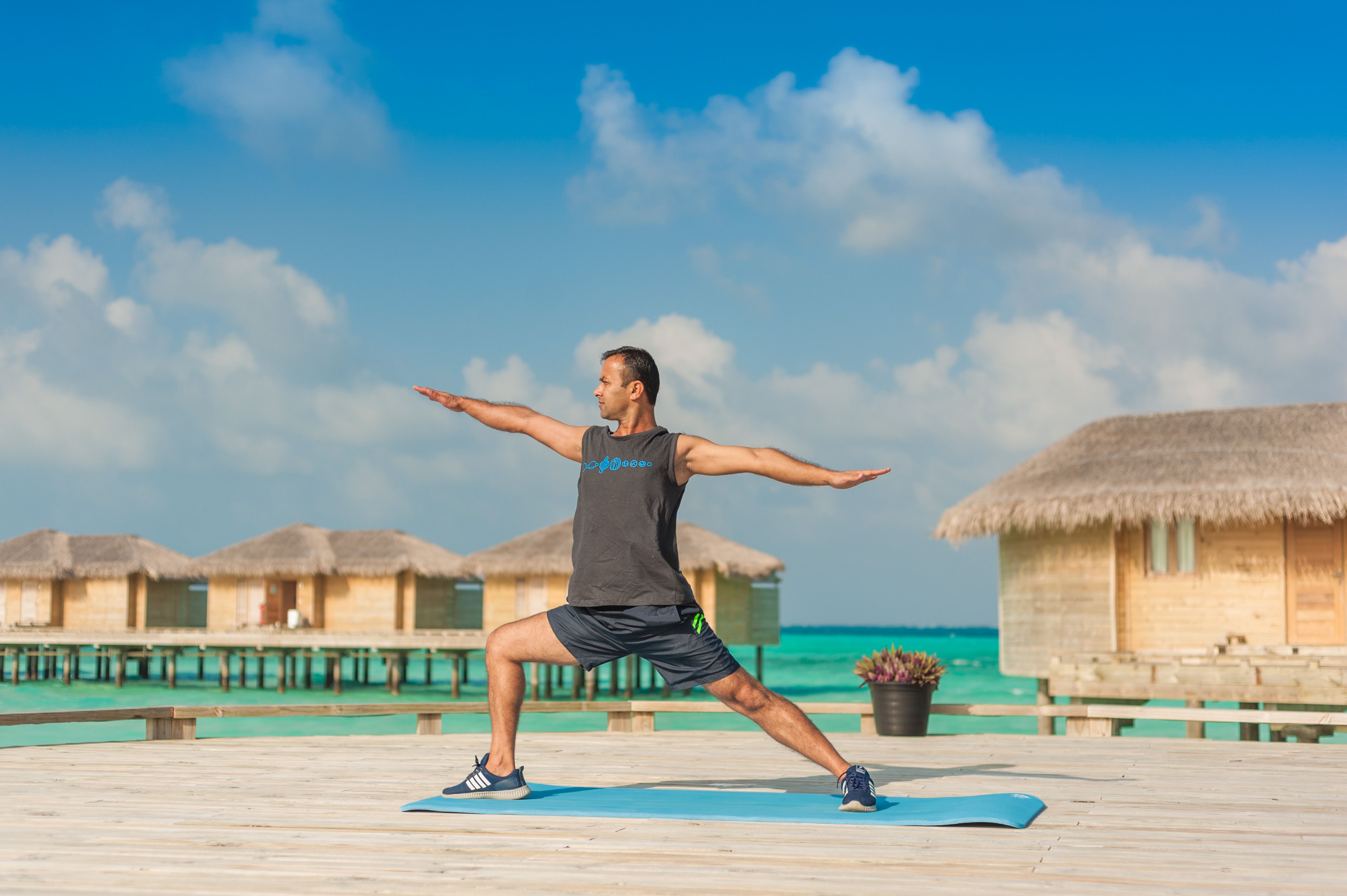 Man stretching in yoga pose on a deck with tropical huts and ocean view.