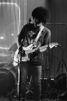 Musician playing electric guitar on stage in moody black and white ambiance.