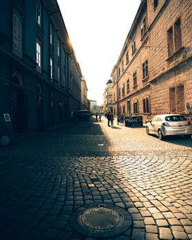 Charming urban street with cobblestones, historic architecture, and parked car in warm lighting.