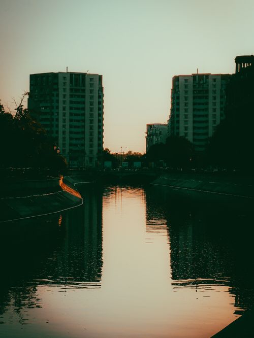 Free Serene urban river scene with high-rise buildings at sunset, reflecting in the calm water. Stock Photo