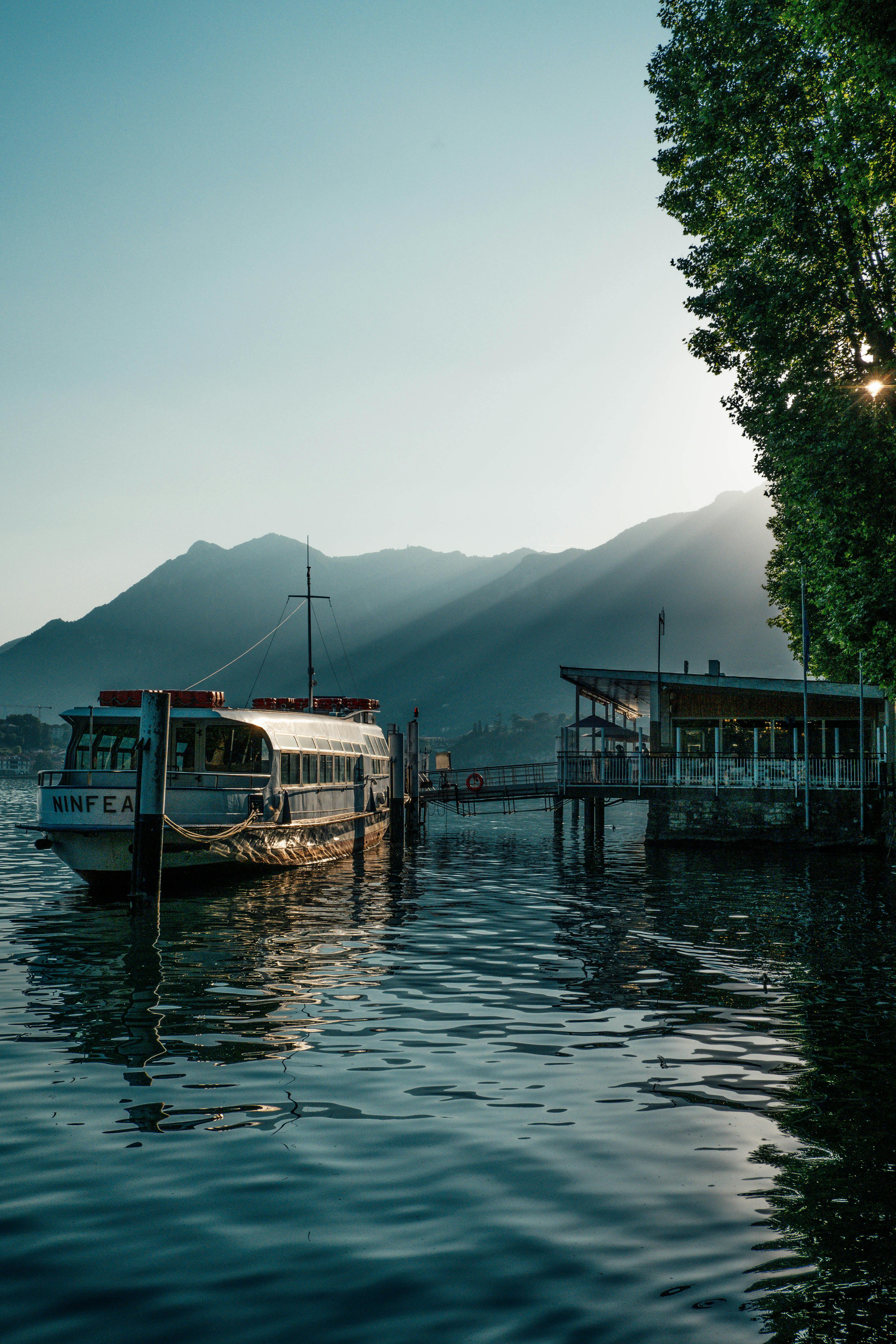 Peaceful morning scene with a docked passenger ship by a lake and mountains