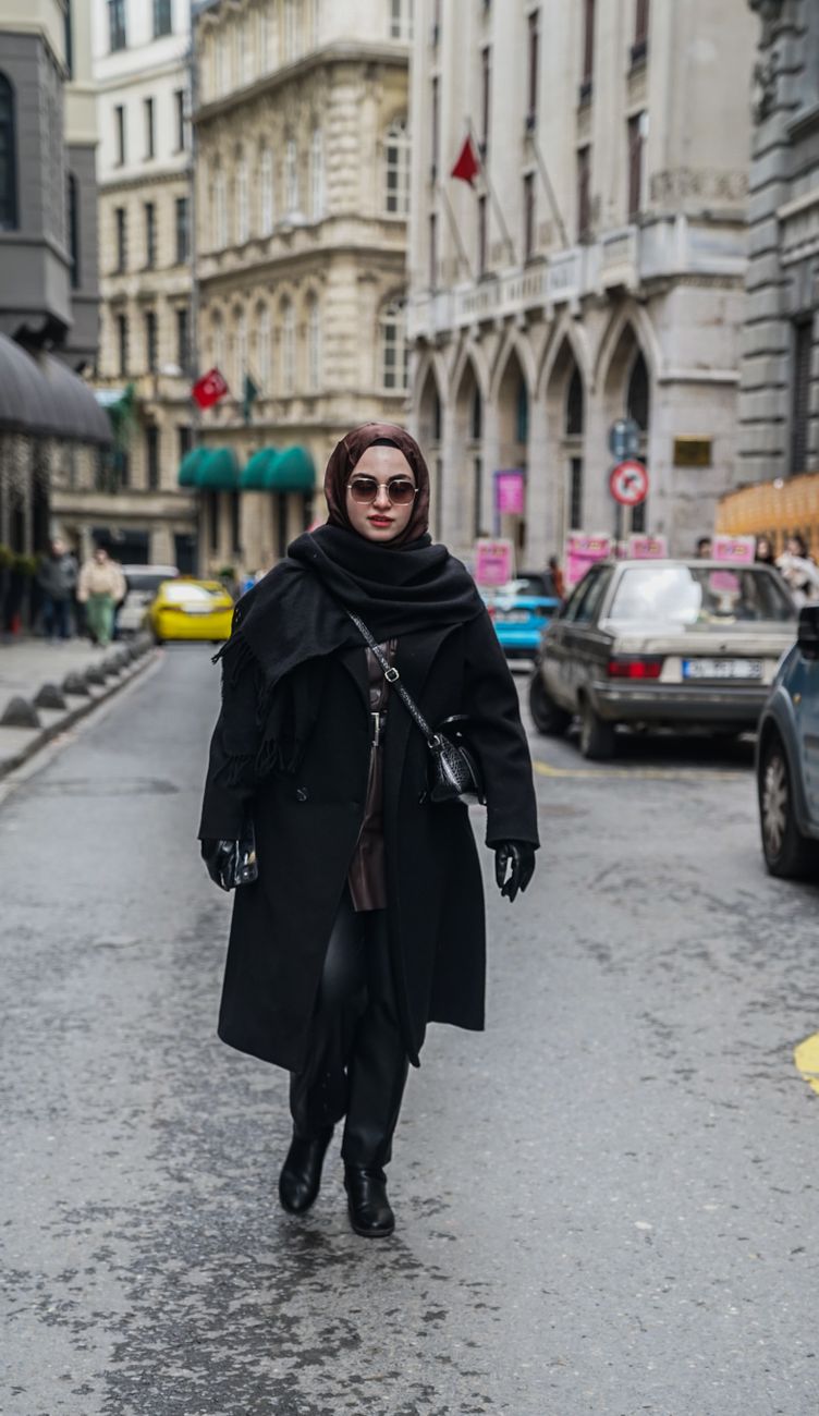 A fashionable woman in a black coat walks confidently down a city street, embodying urban elegance.