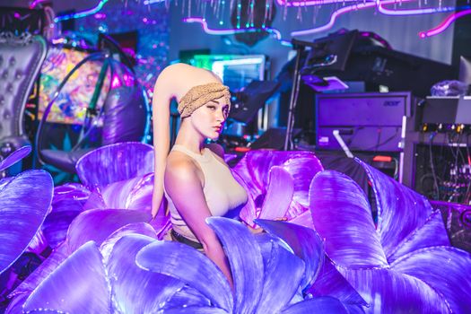 A woman in an elaborate costume poses in a neon-lit environment with vibrant purple decor.