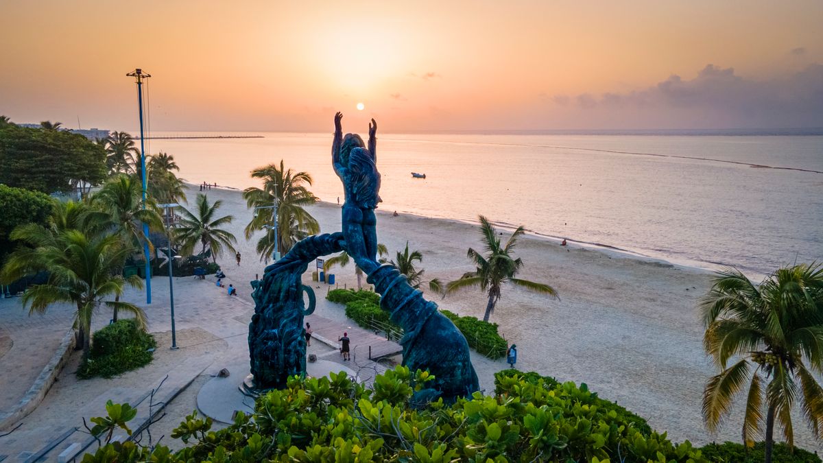 Stunning sunset view at Portal Maya sculpture, Playa del Carmen beachside with palm trees and serene sea.