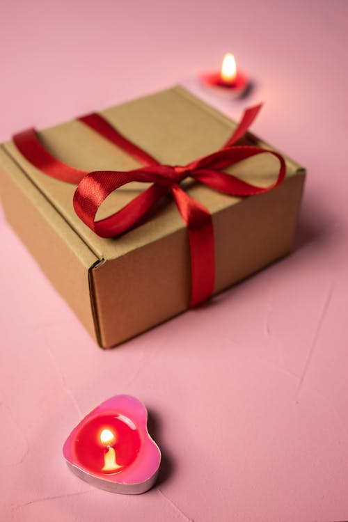 A Gift Box with a Red Ribbon and Burning Heart Shaped Candles 
