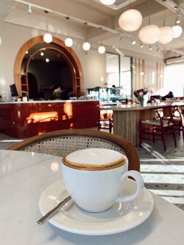A fresh cappuccino on a marble table in a stylish, modern cafe with warm lighting.