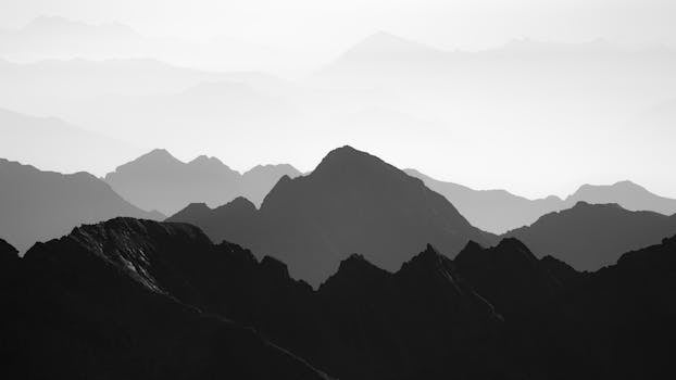Black and white image of layered mountain silhouettes shrouded in mist at dawn.
