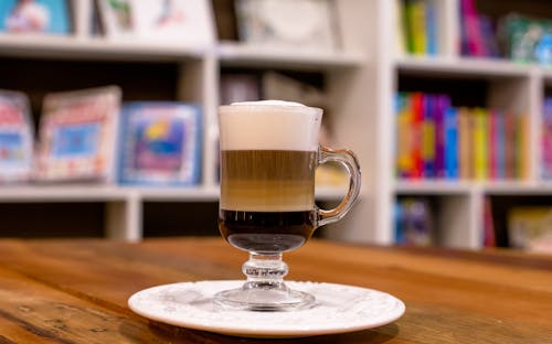 A glass of coffee on a table in front of books
