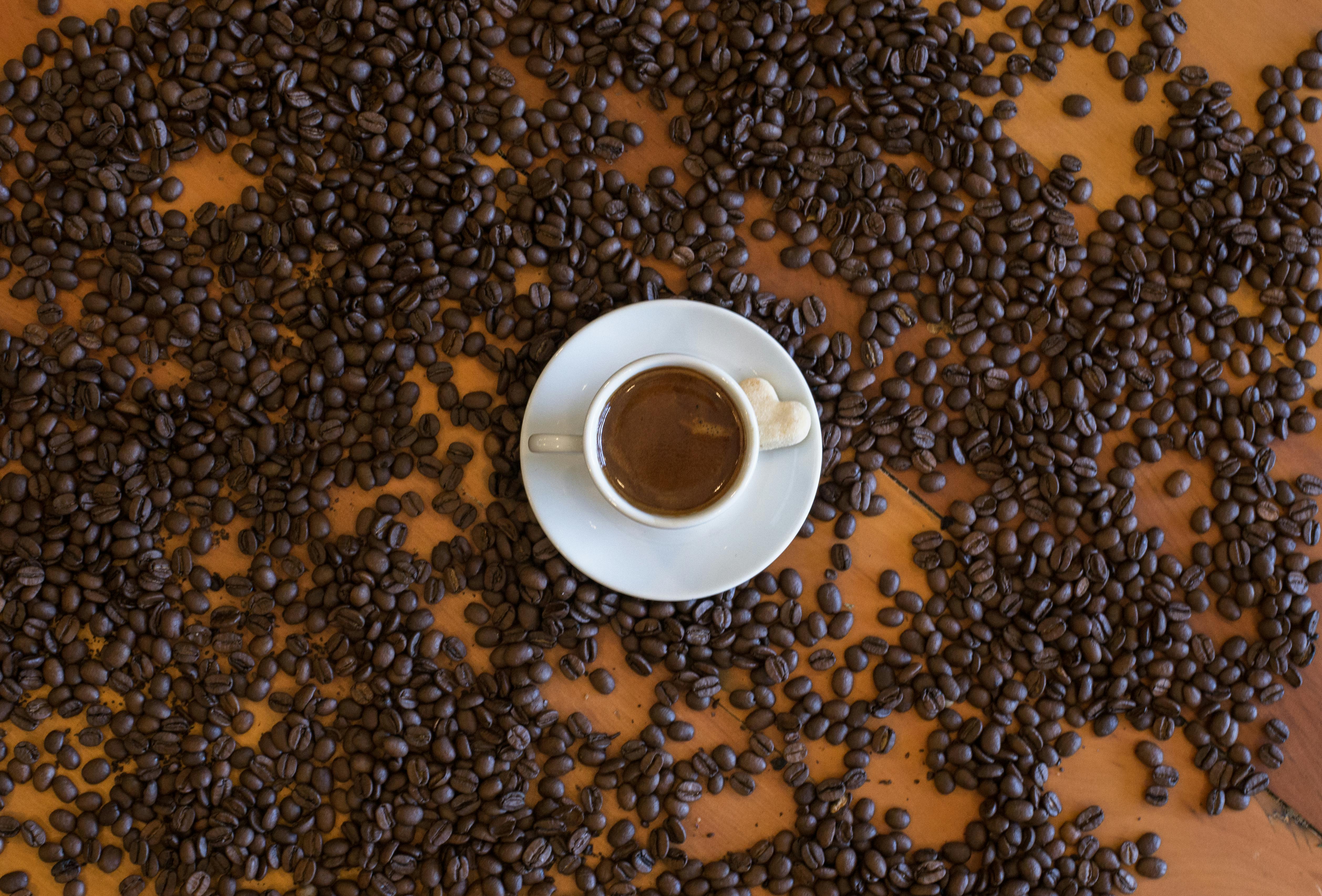 A top view of an espresso cup on a wooden table, surrounded by scattered coffee beans.