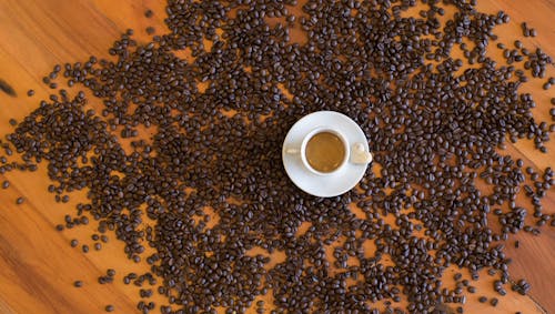 Coffee beans scattered on a wooden table with a cup of coffee