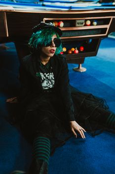 Stylish woman with green hair and sunglasses poses by a pool table, capturing a retro vibe.