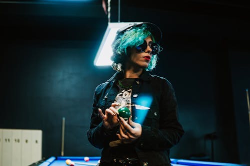Woman with Green Hair Holding a Green Billiard Ball at a Pool Table
