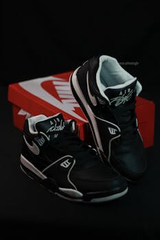 Black sneakers with logo against a dark background, next to branded shoe box.