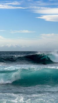 Capture of powerful ocean waves crashing under a serene blue sky, showcasing nature's beauty.