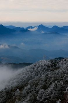 A breathtaking view of a frosted mountain range with mist and clouds against a blue sky.