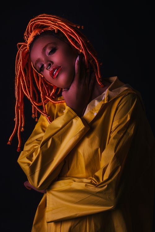 Free Striking studio portrait of a fashionable woman with orange dreadlocks and bright yellow attire. Stock Photo