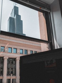 A stunning view of a famous skyscraper seen through an office window with a computer screen in the foreground.