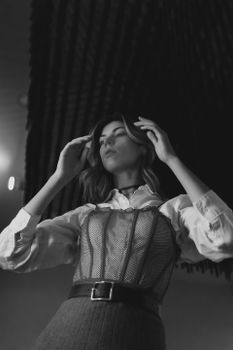 Black and white portrait of a woman posing gracefully with hands near hair in an elegant outfit.