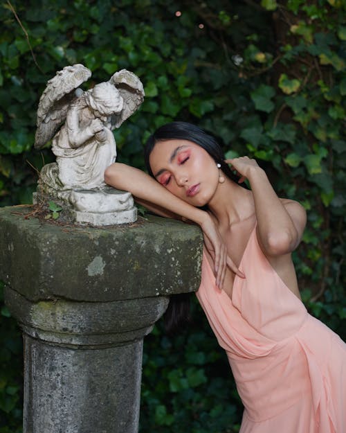 Model in a Pink V-neck Dress Leaning on an Angel Sculpture