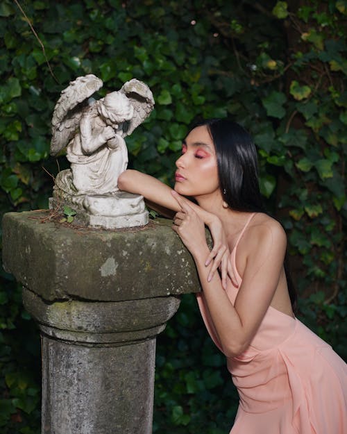 Model in a Pink Backless Dress Standing by an Angel Sculpture