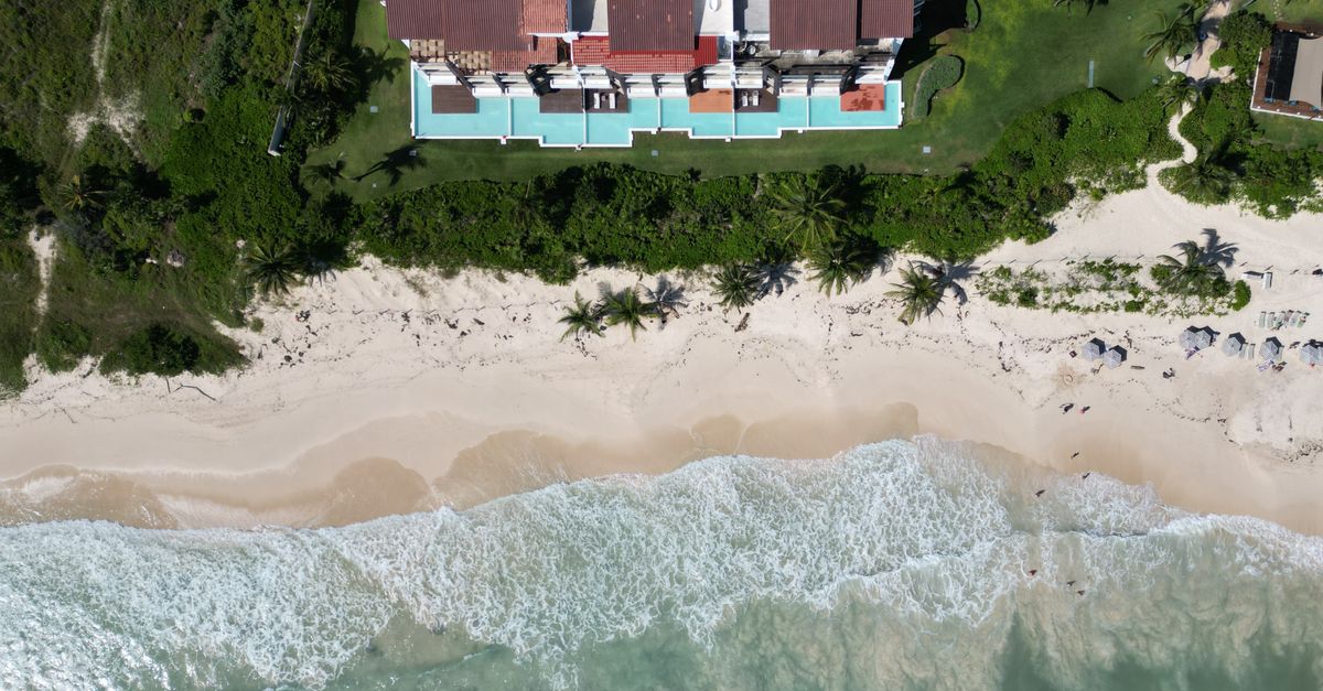 Top-down view of a beachfront mansion with pool and palm trees in Playa del Carmen, México.