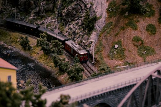 Detailed miniature model of a train on a scenic bridge surrounded by rocky and green landscape.