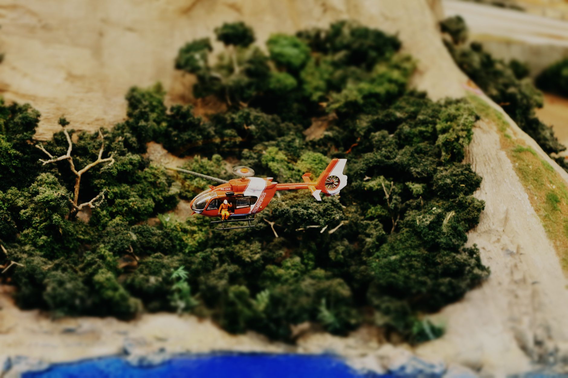 A detailed model helicopter flies over a lush forest diorama, capturing the essence of adventure.