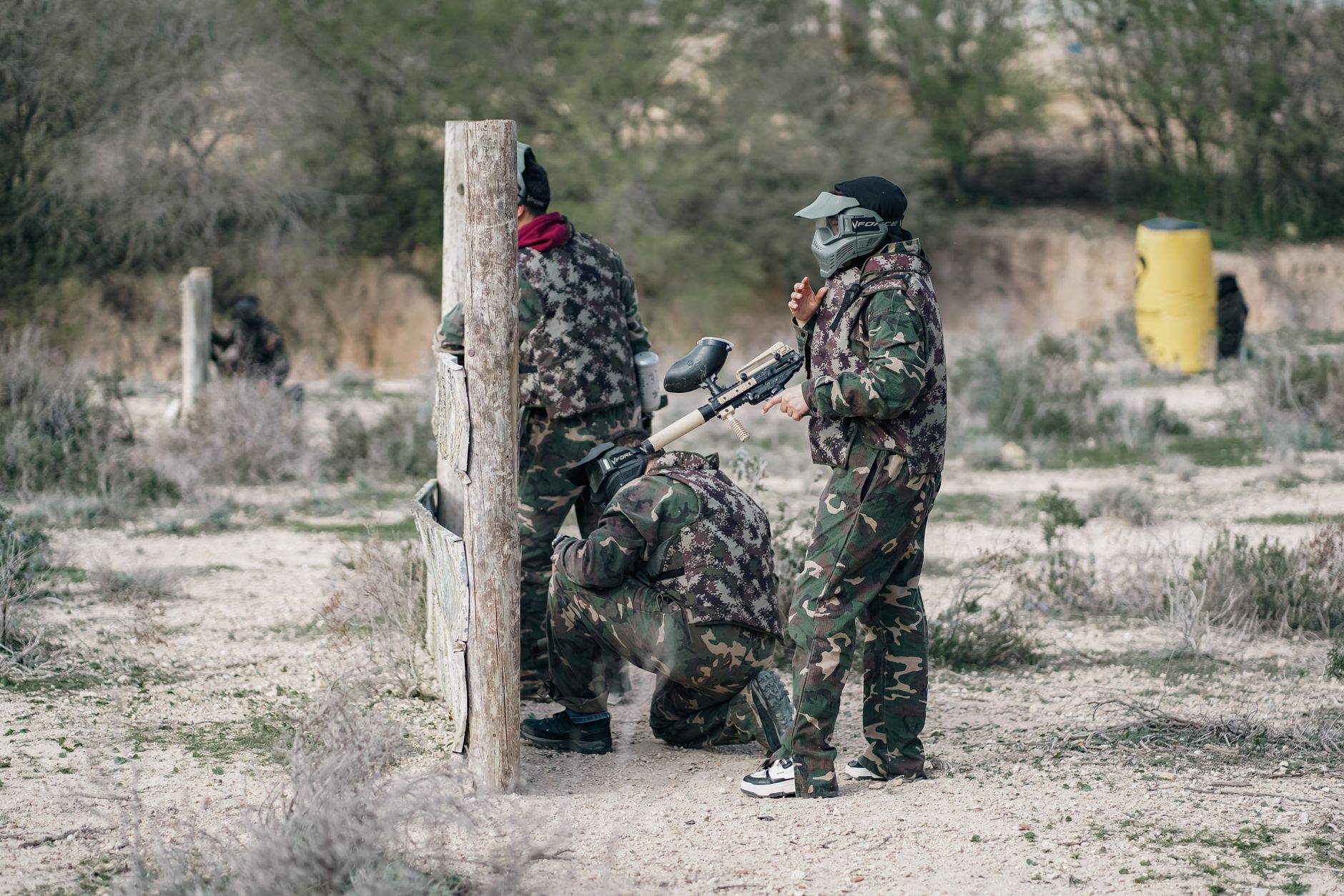 Group of adults in camouflage gear playing paintball outdoors for recreation.