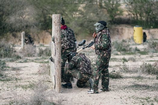 Group of adults in camouflage gear playing paintball outdoors for recreation.