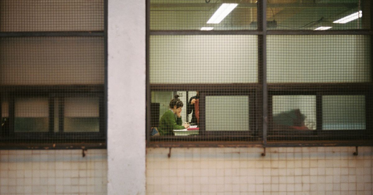 Vista de personas trabajando dentro de una oficina vista a través de una gran rejilla de ventana industrial.