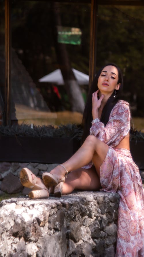 Young, Elegant Woman in a Dress and Heels Sitting on a Wall Outside 