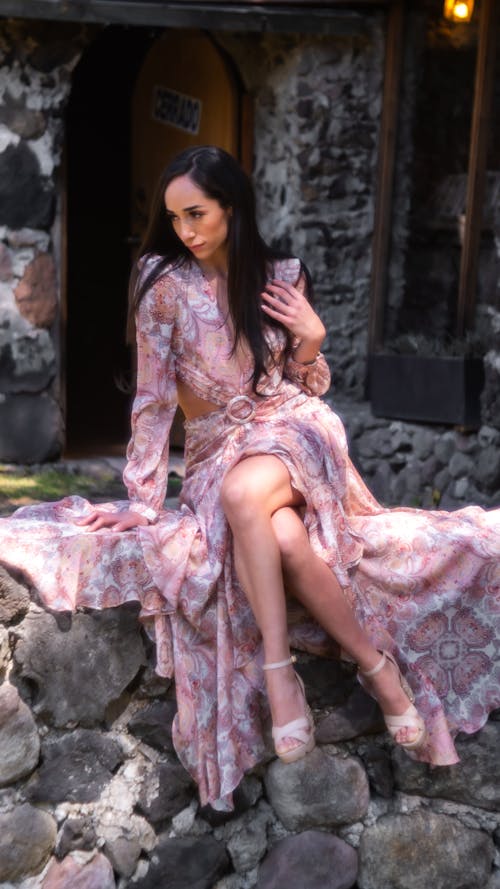 Young, Elegant Woman in a Dress and Heels Sitting on a Wall Outside 