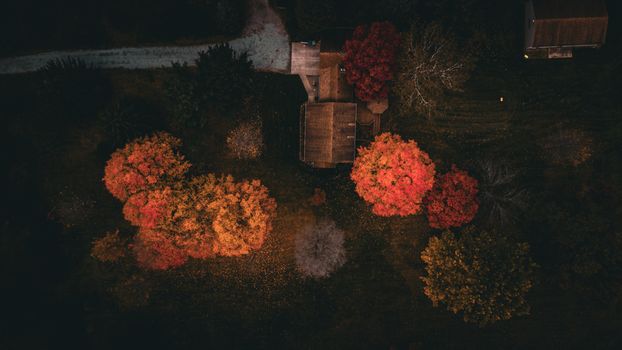 Scenic aerial shot of fall foliage surrounding houses in a dark countryside setting.