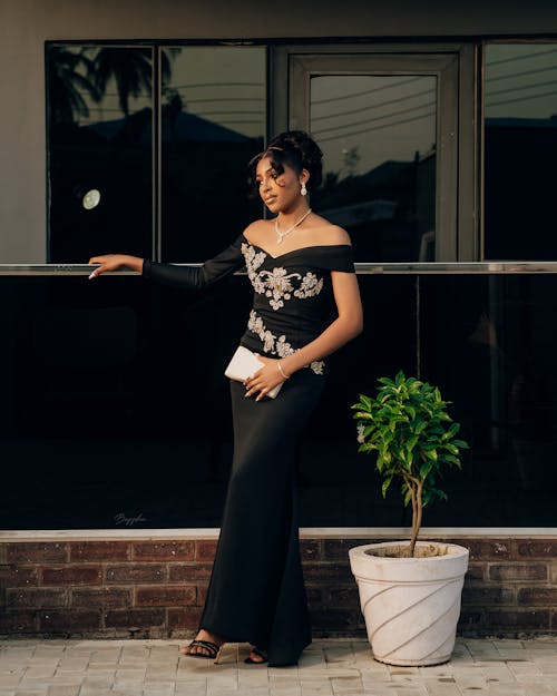 A woman in a black dress and heels standing next to a plant