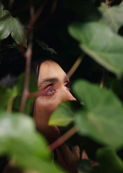 Free A woman looks upwards through vibrant green leaves, capturing natural beauty and introspection. Stock Photo