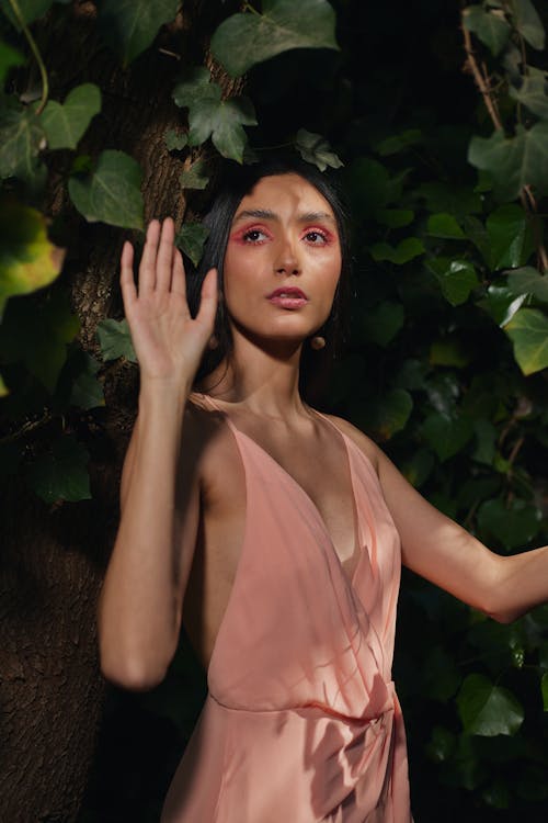 Young Woman in a Pink Dress Standing under a Tree and Waving 