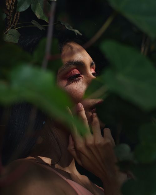 Free A mysterious woman peers through vibrant green leaves, showcasing natural beauty and serenity. Stock Photo