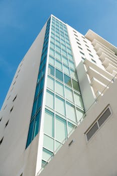 Low angle view of a modern high-rise building featuring glass windows under a clear blue sky.