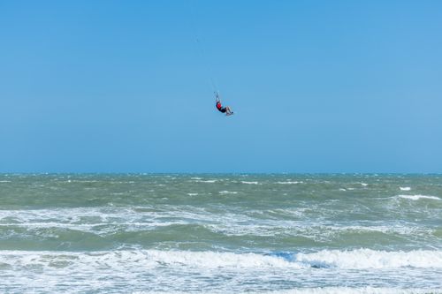 Free High-flying kitesurfer against the clear blue sky over the ocean, showcasing extreme sports action. Stock Photo