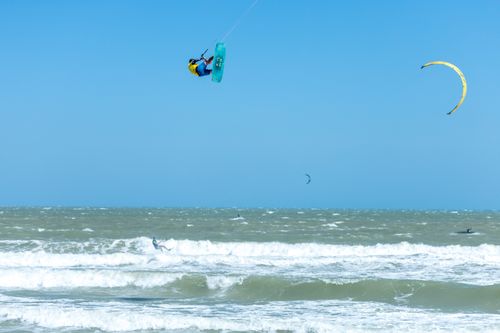 Free Kitesurfer executing a dramatic aerial stunt over ocean waves under a clear blue sky, showcasing extreme sports action. Stock Photo