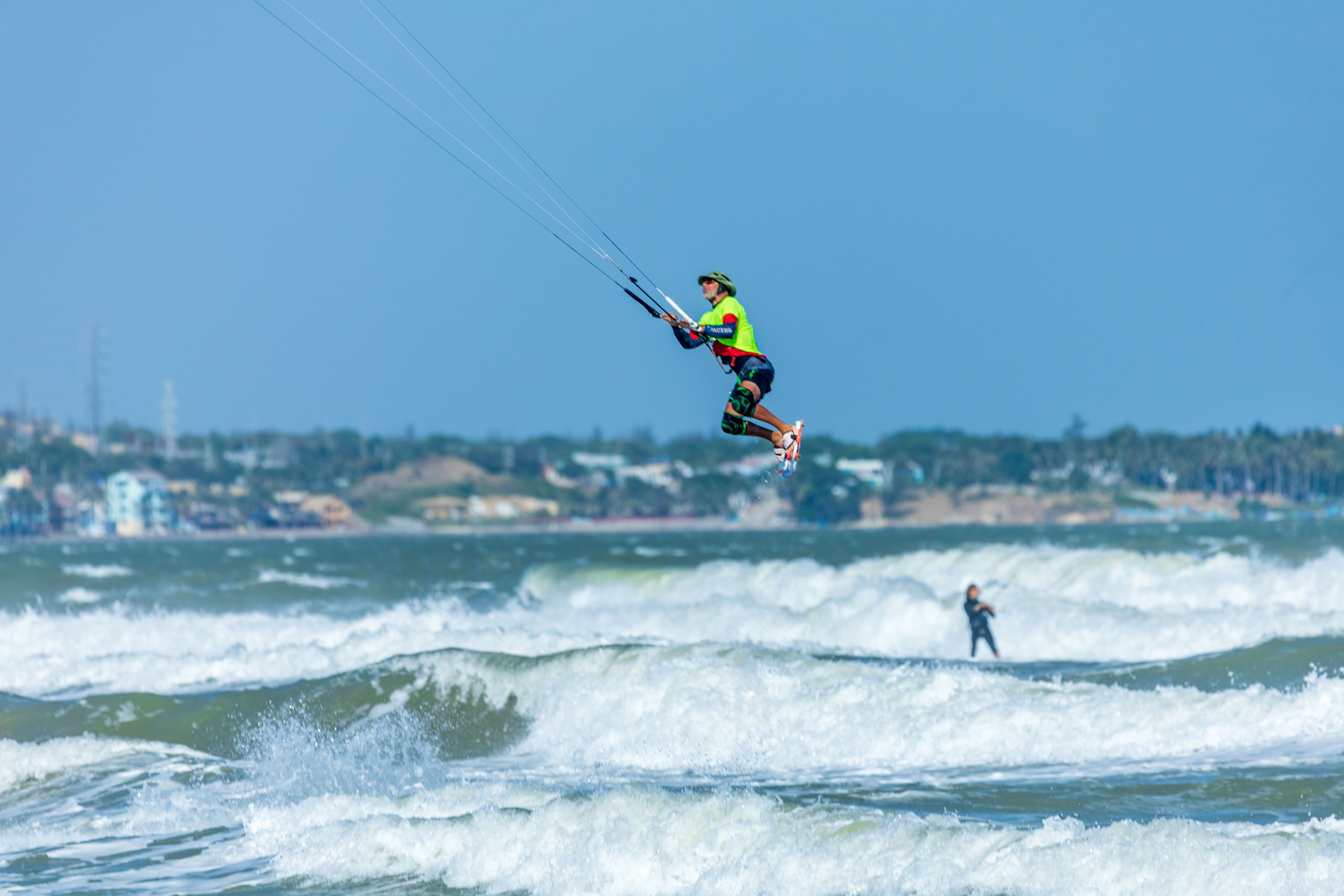 Capturing a kitesurfer mid-air above the ocean's waves against a coastal backdrop.