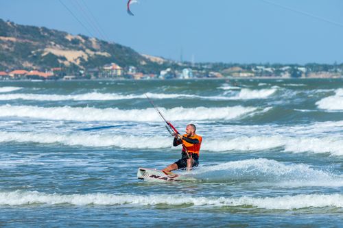 Free A man enjoying kiteboarding on a sunny beach, riding the waves actively. Stock Photo