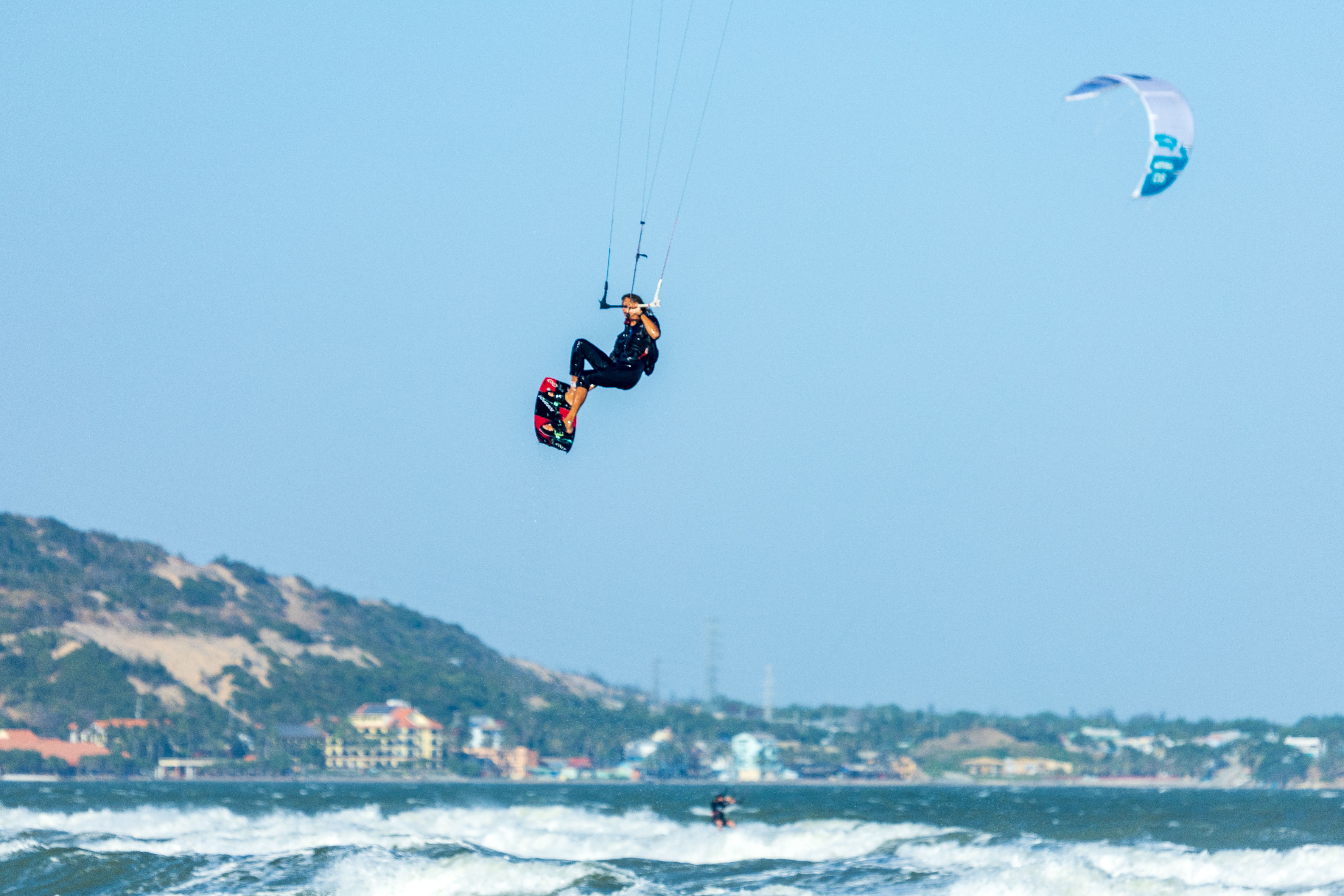 A kitesurfer skillfully jumps over ocean waves against a clear blue sky, showcasing thrilling outdoor adventure sports.