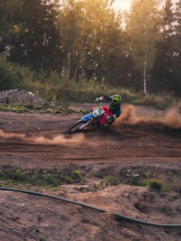 越野摩托车骑手在树木环绕的土路上疾驰，扬起阵阵灰尘，展现了速度与敏捷