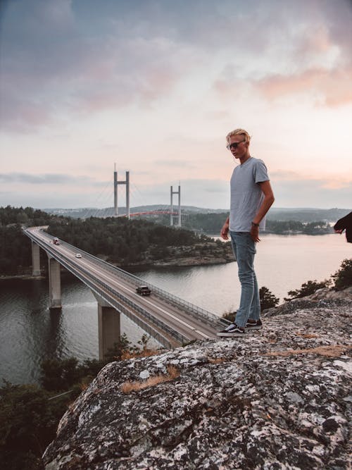 Man Stands on Crest of Hill Overlooking Bridge