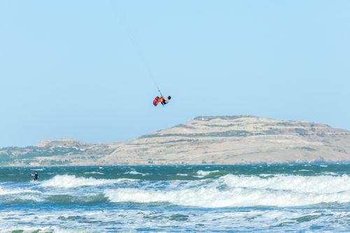Free Dynamic shot capturing a kitesurfer executing high jumps above ocean waves with a hilly backdrop. Stock Photo